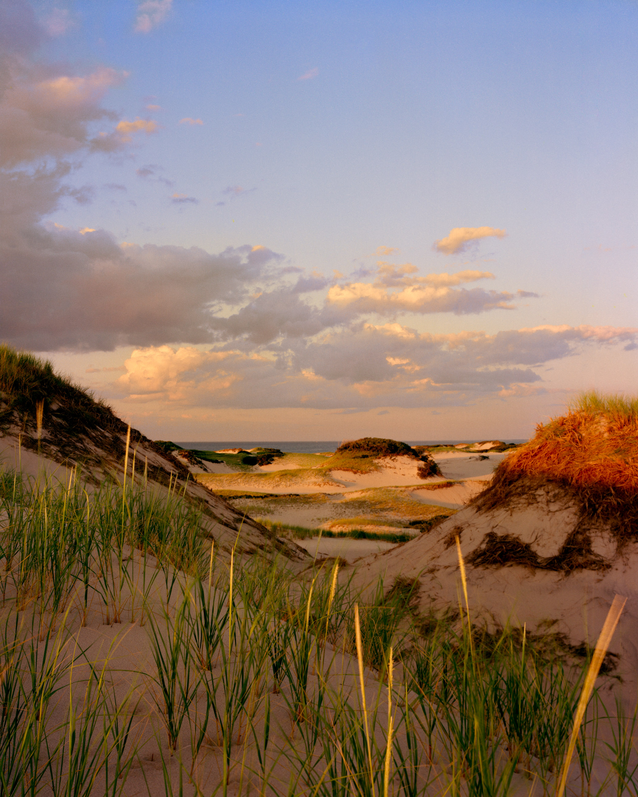 This three-panel panoramic landscape photograph made on Cape Cod depicts golden sunset light washing over sand dunes crested with American beachgrass below a dramatic sky.