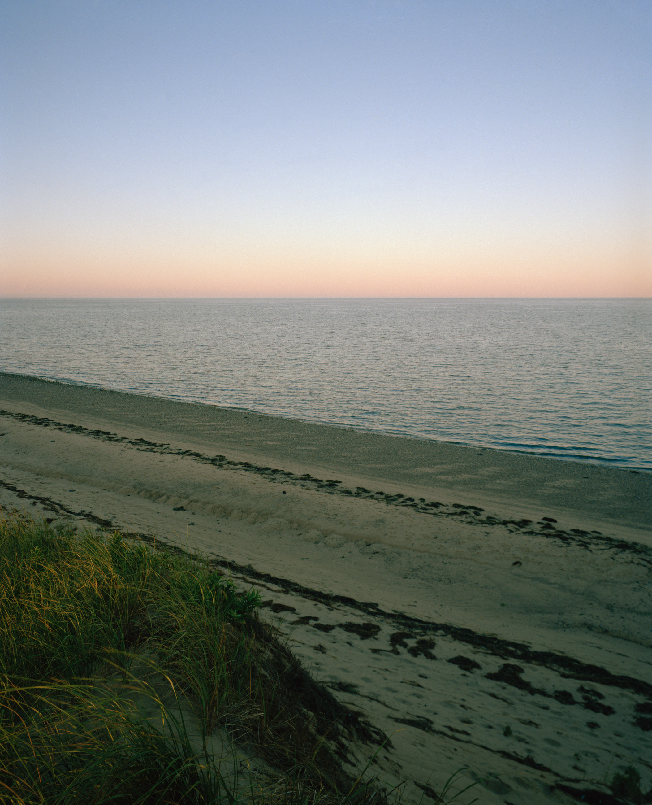 This seven-panel panoramic Cape Cod beach landscape photograph shows the light from a sunrise falling across a spit of beach projecting into a bay.