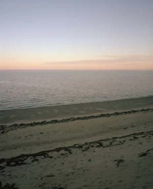 This seven-panel panoramic Cape Cod beach landscape photograph shows the light from a sunrise falling across a spit of beach projecting into a bay.