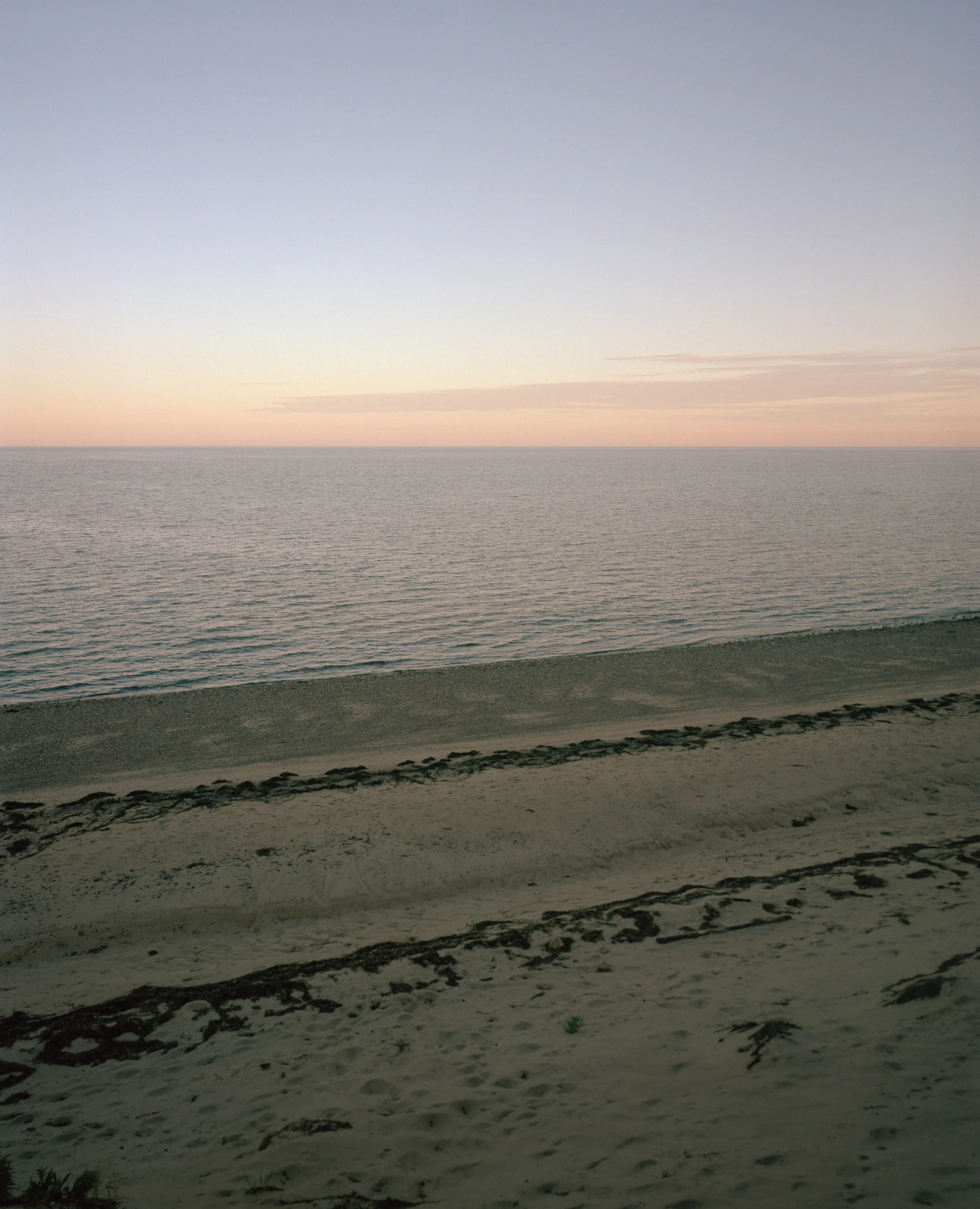This seven-panel panoramic Cape Cod beach landscape photograph shows the light from a sunrise falling across a spit of beach projecting into a bay.