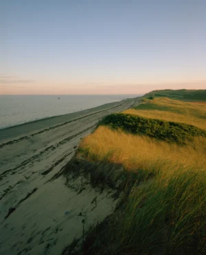 This seven-panel panoramic Cape Cod beach landscape photograph shows the light from a sunrise falling across a spit of beach projecting into a bay.