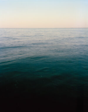 This five-panel panoramic landscape photograph shows flooding Cape Cod Bay tidal water rising up around a field of boulders distributed across a small beach headland.