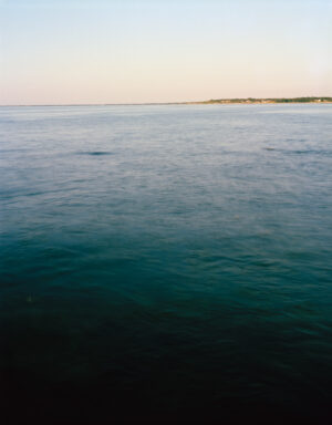 This five-panel panoramic landscape photograph shows flooding Cape Cod Bay tidal water rising up around a field of boulders distributed across a small beach headland.