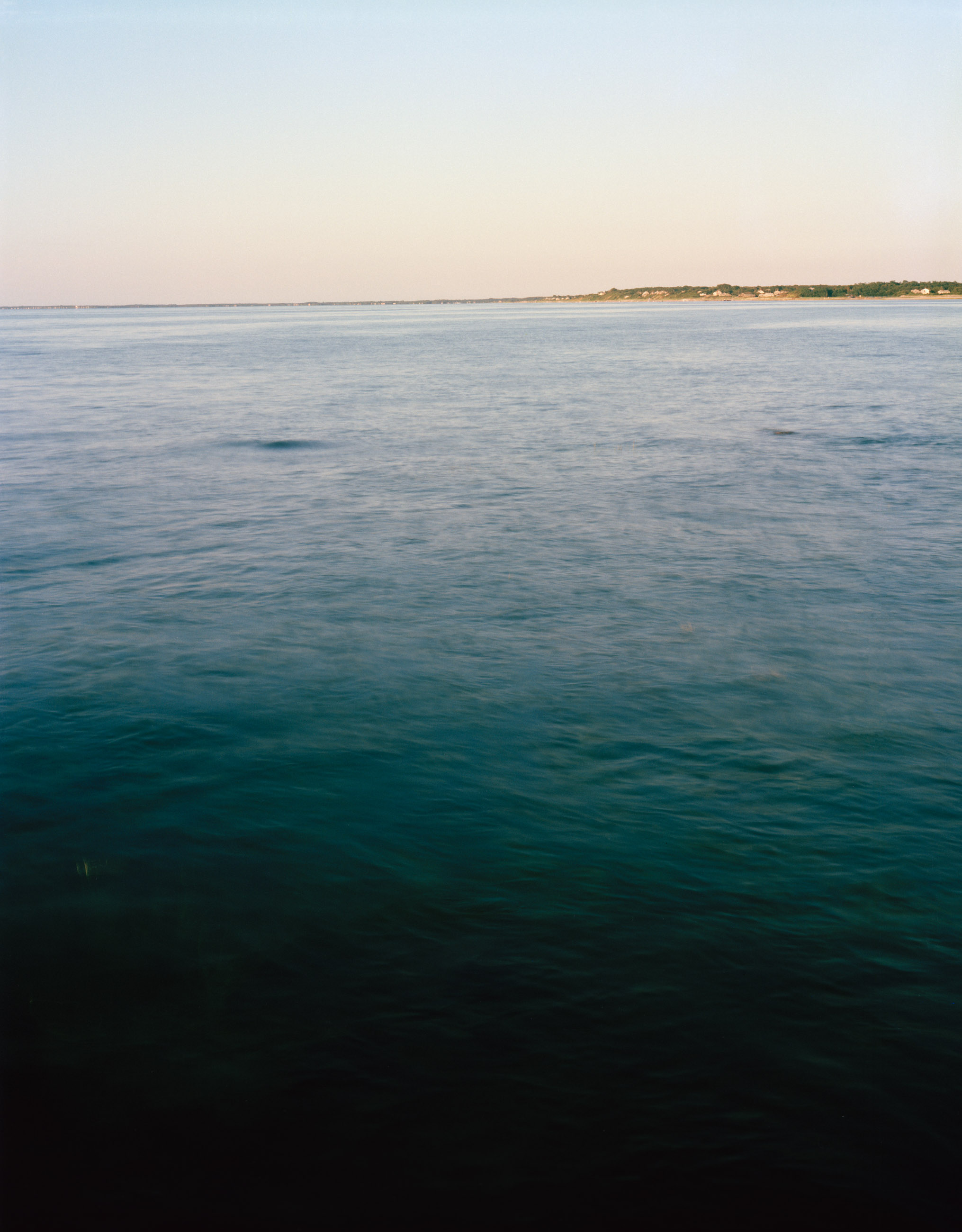 This five-panel panoramic landscape photograph shows flooding Cape Cod Bay tidal water rising up around a field of boulders distributed across a small beach headland.