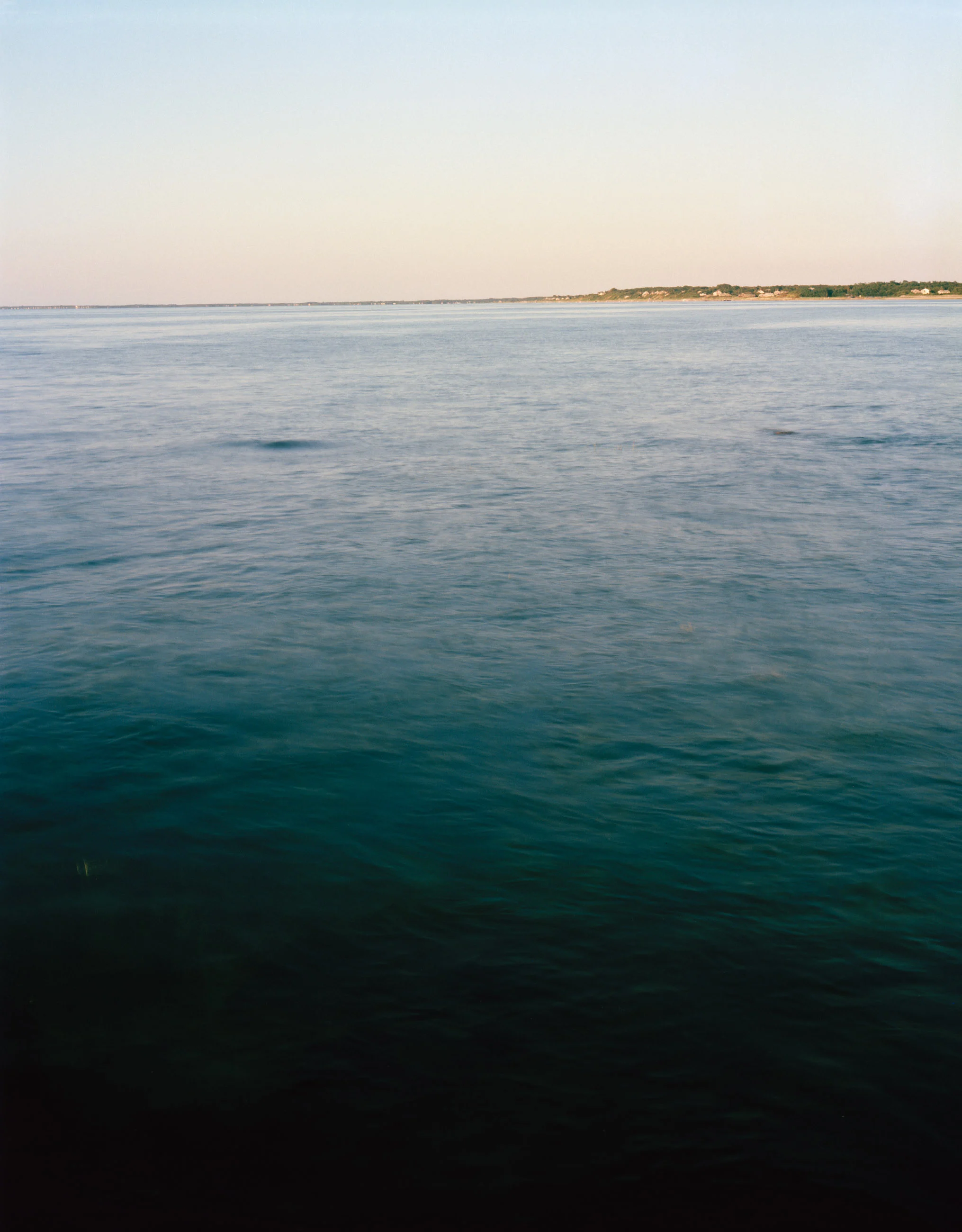 This five-panel panoramic landscape photograph shows flooding Cape Cod Bay tidal water rising up around a field of boulders distributed across a small beach headland.