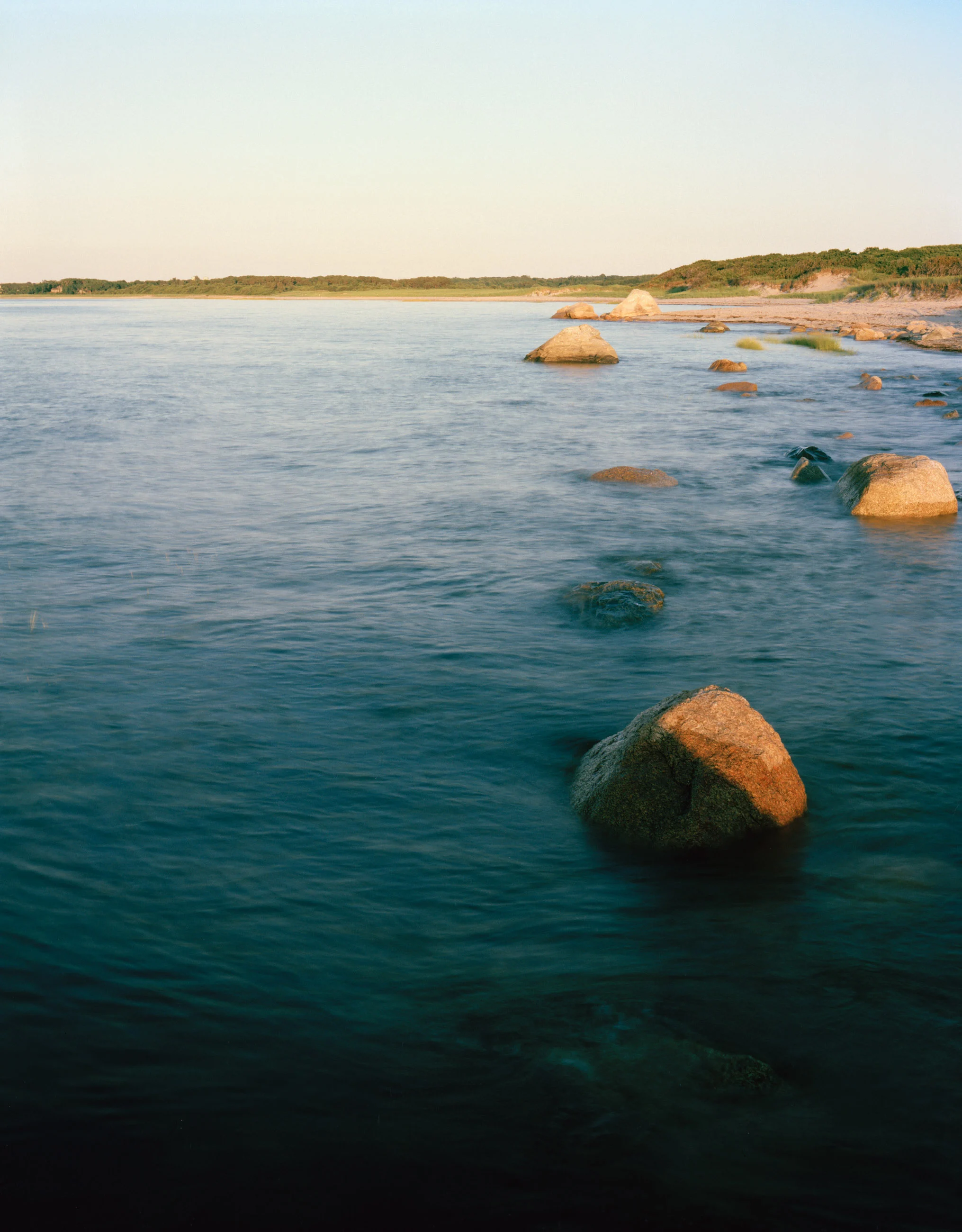 This five-panel panoramic landscape photograph shows flooding Cape Cod Bay tidal water rising up around a field of boulders distributed across a small beach headland.