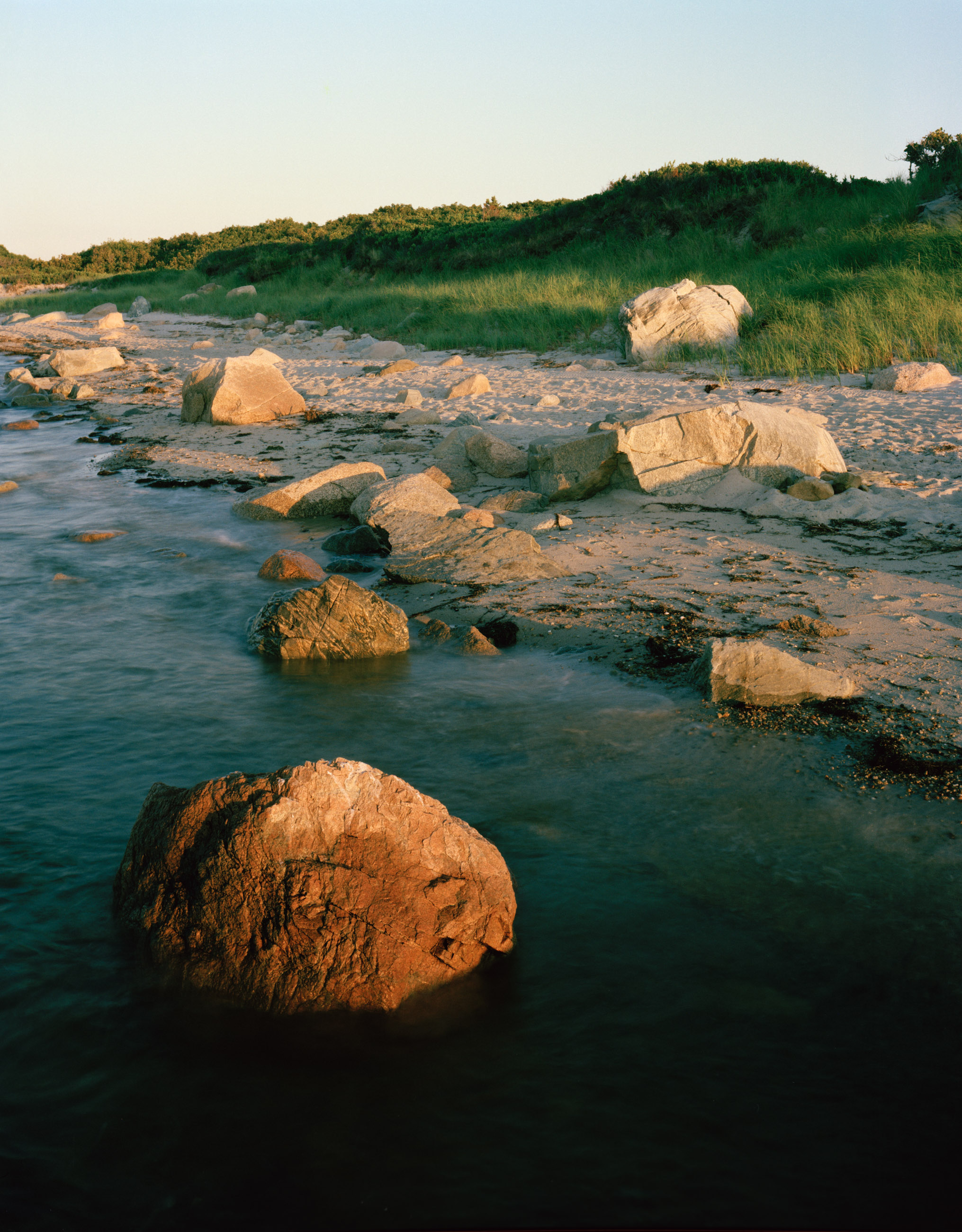 This five-panel panoramic landscape photograph shows flooding Cape Cod Bay tidal water rising up around a field of boulders distributed across a small beach headland.
